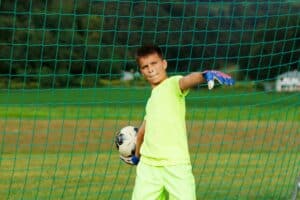 A young goalkeeper throws the ball away from the goal